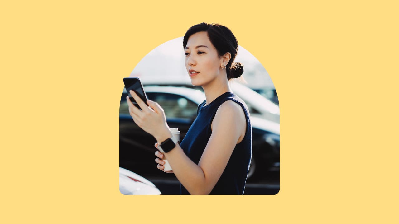 An east Asian woman looking at her phone while at a car lot. Image is on a yellow background.
