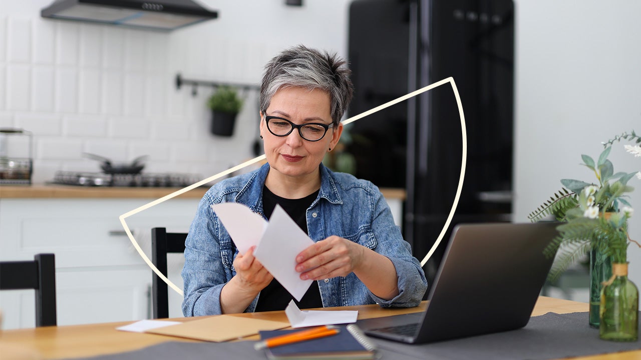 An older woman with black glasses on reviews papers at her table. There is an illustrated semicircle behind her.