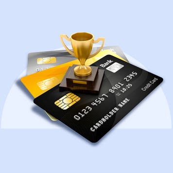 A tiny golden cup trophy standing on three fanned out credit cards.