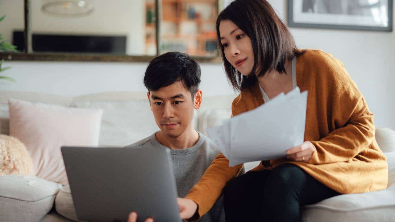 Serious looking young couple discussing over financial bills while using laptop in living room.