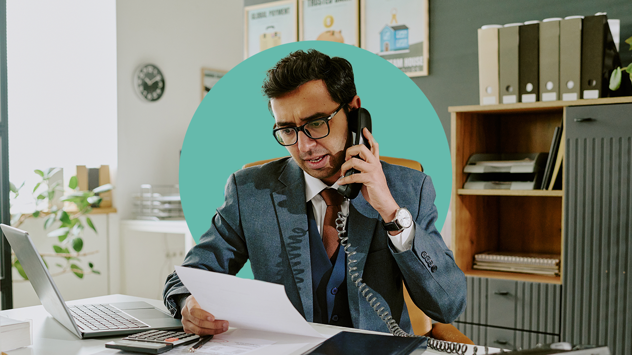 person on phone by computer looking at piece of paper