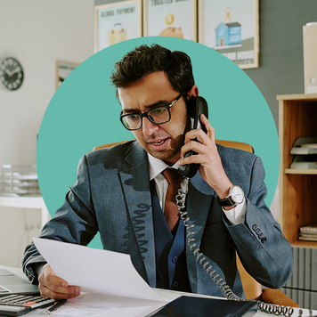 person on phone by computer looking at piece of paper