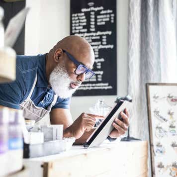 Storeowner leans over counter looking at tablet.