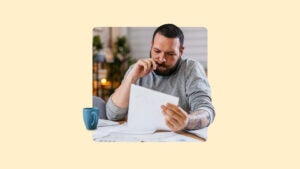 Man reviewing paper with green mug next to him.