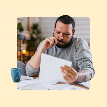 Man reviewing paper with green mug next to him.