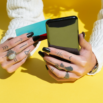 Woman's Hands using credit card for shopping online on her smartphone Over Yellow Background