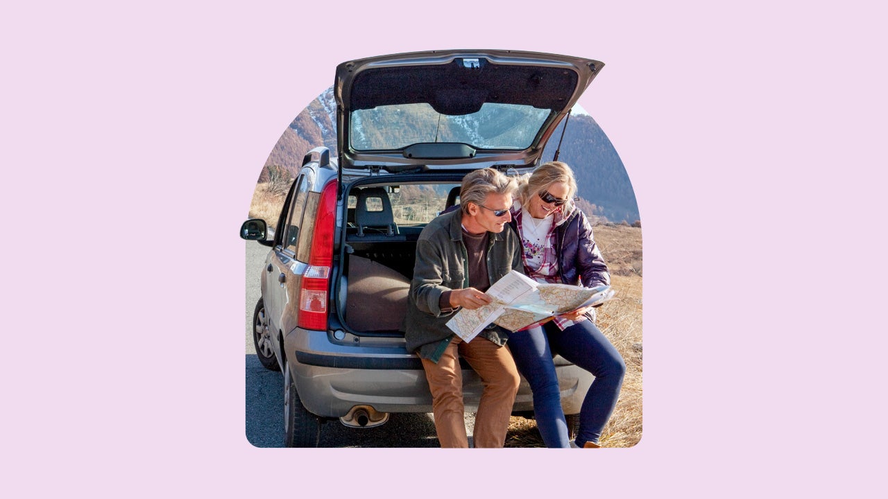 A white couple sits in the back of an SUV while reading a map.