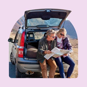 A white couple sits in the back of an SUV while reading a map.