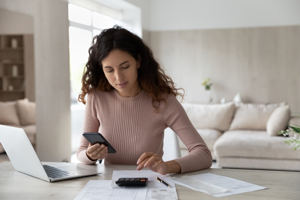 Latino woman calculating her bills in front of a laptop and sitting at a table