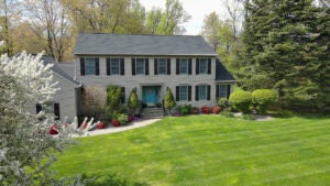 A two-story house and colorful blooming trees on a green lawn in sunny spring season