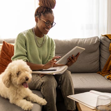 Woman working on a tablet with a dog sitting next to her