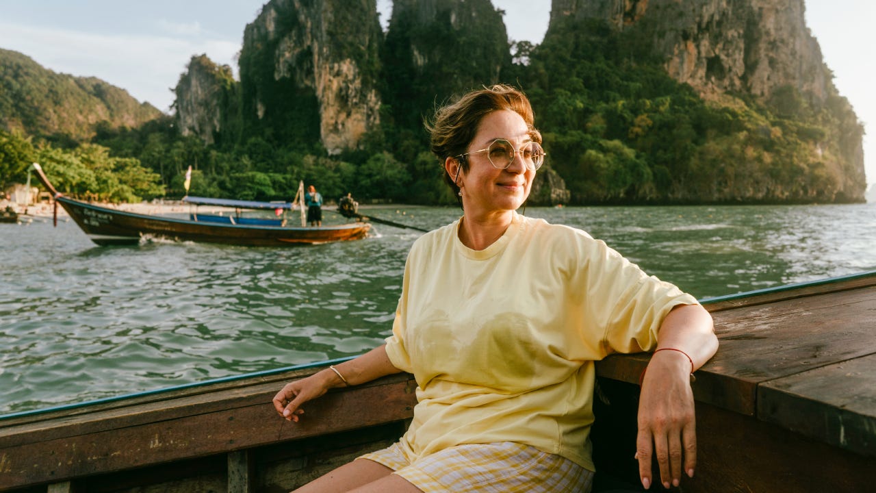 woman of pre-retirement age in sunglasses and a yellow T-shirt sitting on board a wooden boat.