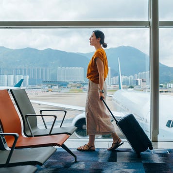 woman carrying suitcase, walking by the window at airport terminal