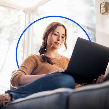a woman sits on her couch with her laptop