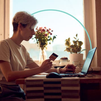Design element of a person sitting in front of a window using a laptop while holding a credit card in hand