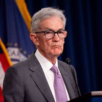Federal Reserve Chair Jerome Powell standing at a lectern with an American flag in the background.