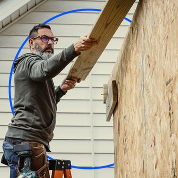 An older white man in glasses putting a board up on a structure with an illustrated blue circle behind him.