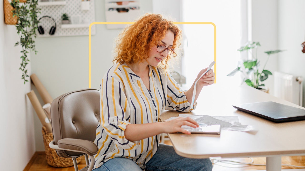 Red haired woman reading bill at desk.