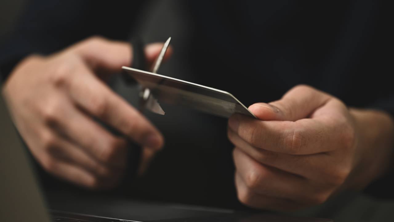 Young man cutting credit card with scissors