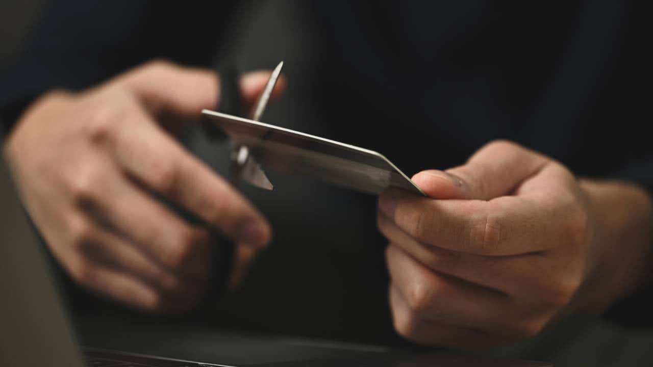 Young man cutting credit card with scissors