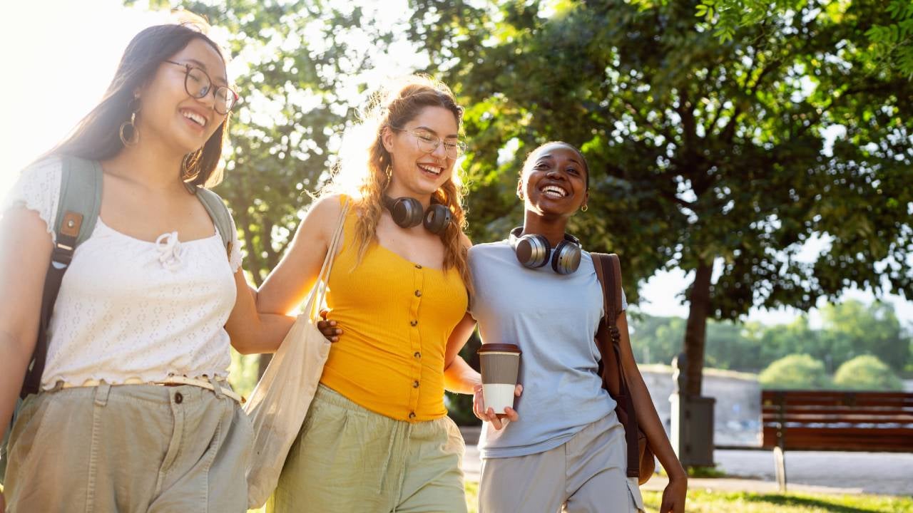 Group of modern young multiracial female friends, an University students, walking through the campus park