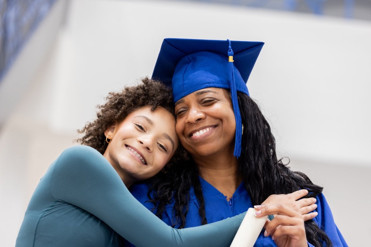 Adult graduate poses for photo with her preteen daughter on graduation day