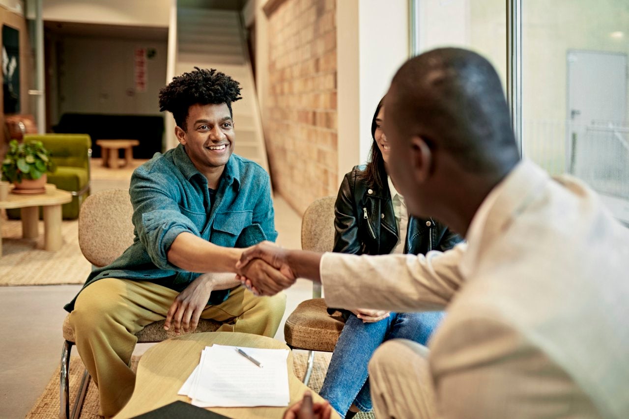 Mid adult sitting and smiling as a bank lender congratulates the man with a handshake