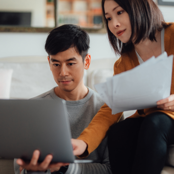 Young couple discussing financial bills while using laptop on sofa.