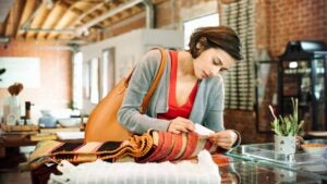 Young woman in a shop, looking at the price tag of a small striped rug.