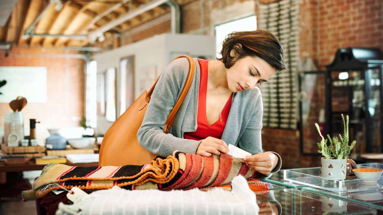 Young woman in a shop, looking at the price tag of a small striped rug.