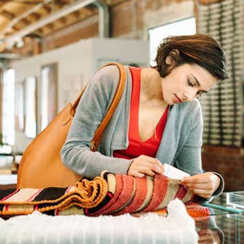 Young woman in a shop, looking at the price tag of a small striped rug.