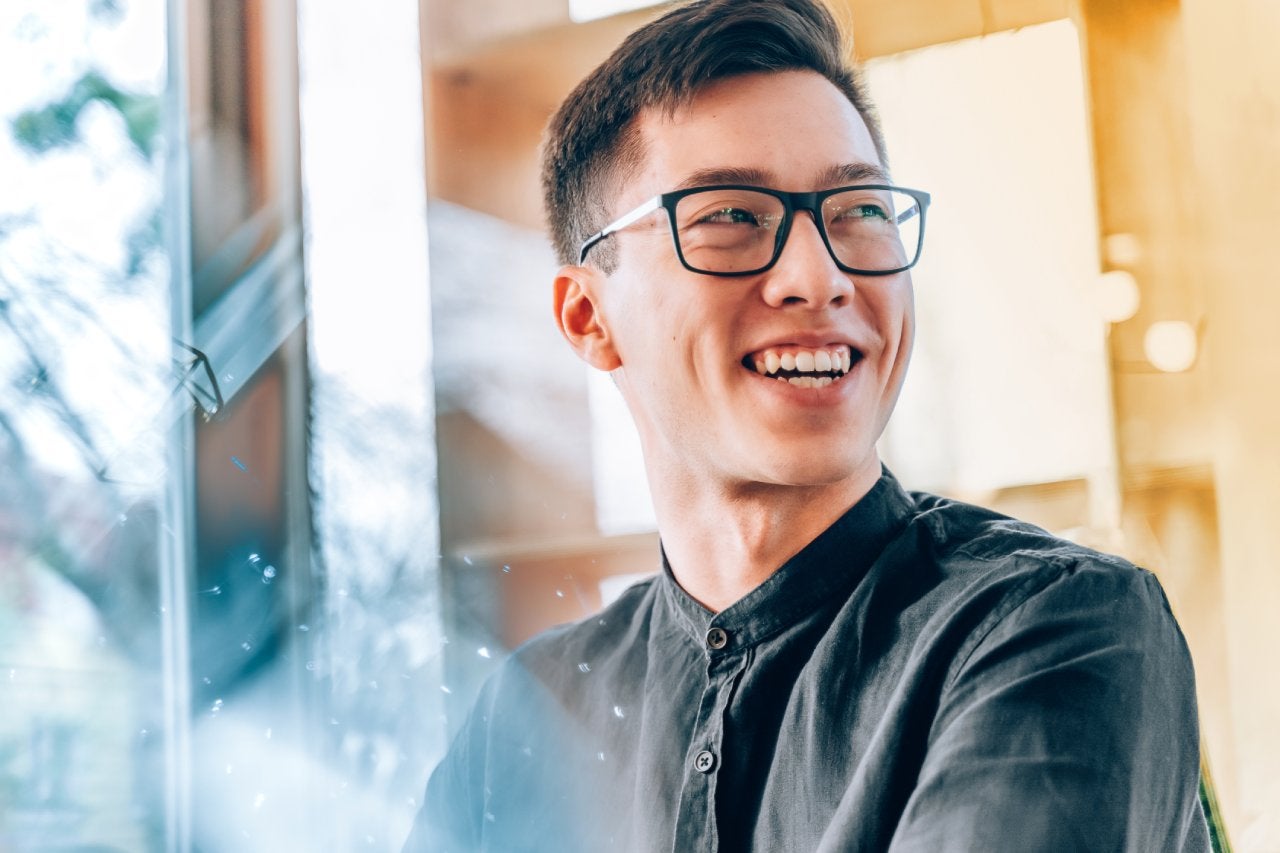 Asian man with glasses smiling off to the side, looking off into the distance