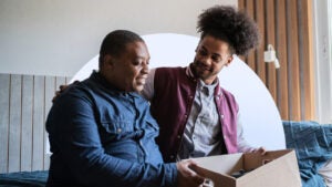 Parent and son sitting on a college dorm bed