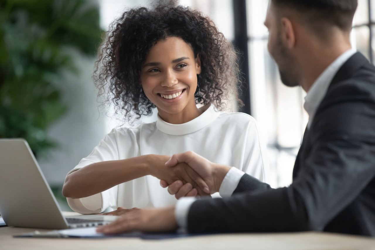 Happy loan manager shaking hands with client in modern office