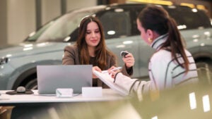 Two women complete paperwork at a dealership.