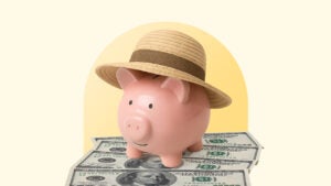 A piggy bank wearing a hat sits on top of cash.