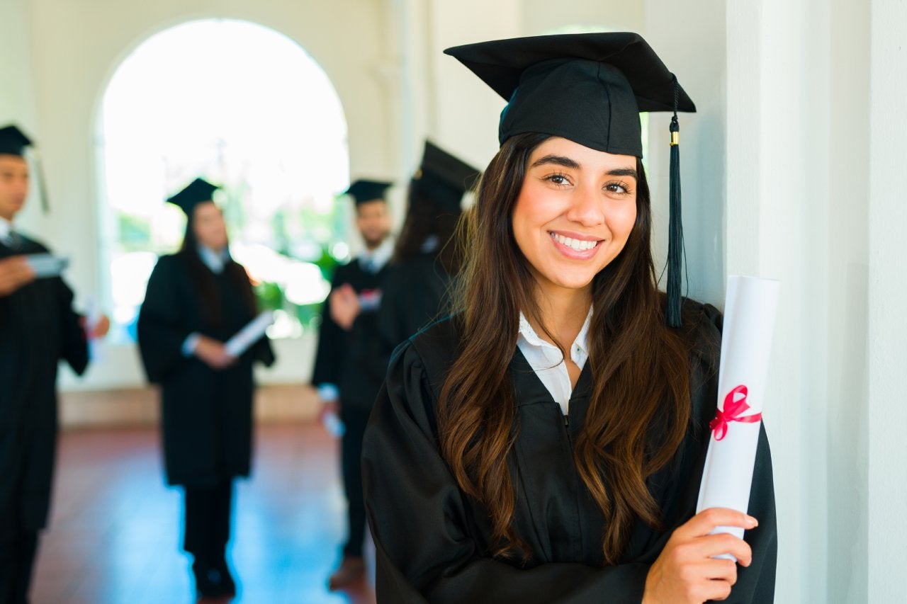 Hispanic woman smiling and making eye contact after getting her university diploma at a graduation ceremony on campus