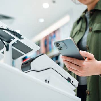 Close up of a person's hand making mobile payment with a smartphone at a self-checkout counter.,
