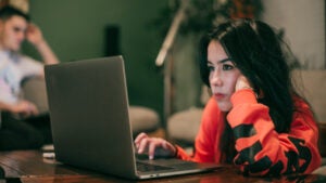 Young woman looks thoughtfully at laptop.