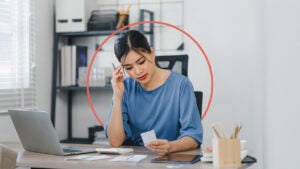 Young woman reviewing her finances at home with an illustrated orange circle behind her.