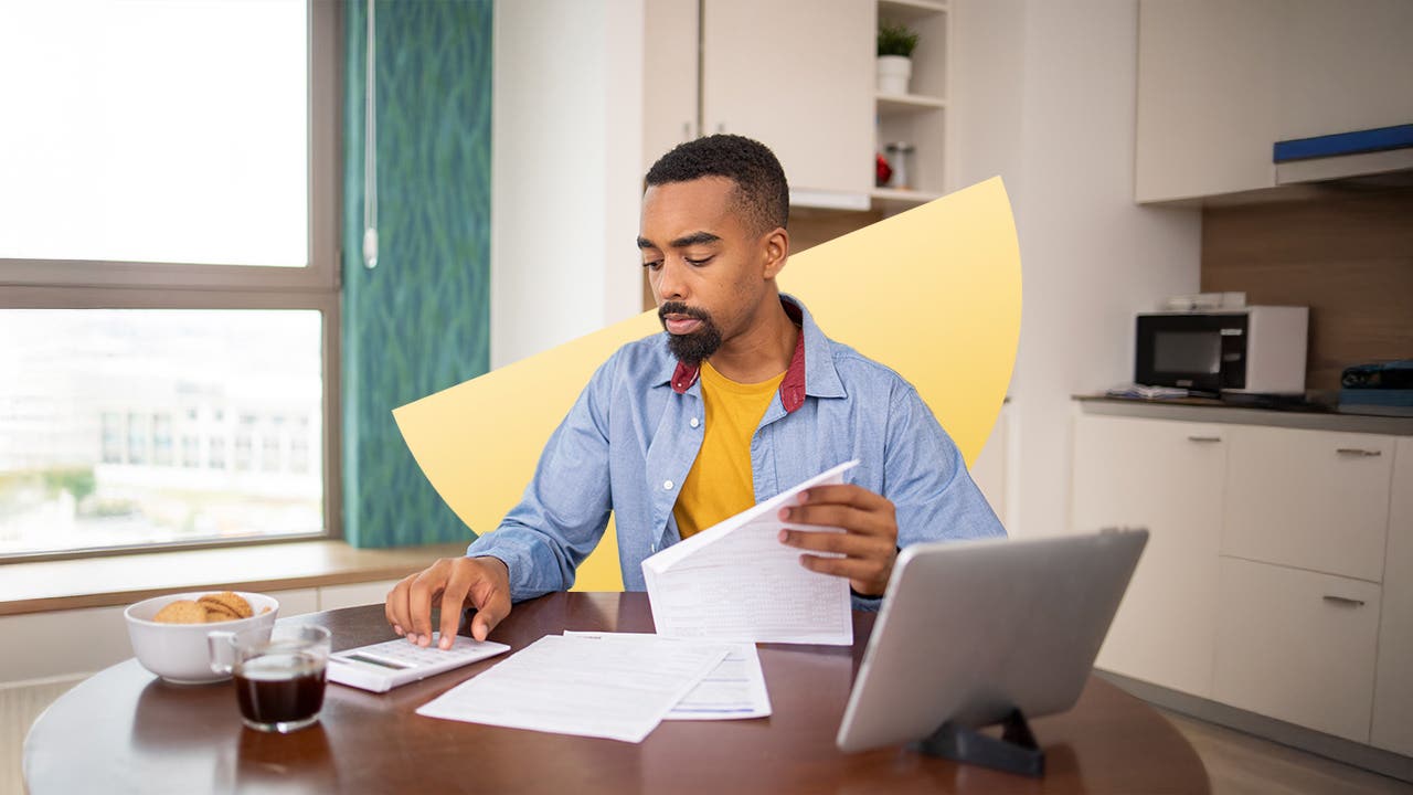 Young Black man uses a calculator at his table while looking through papers.