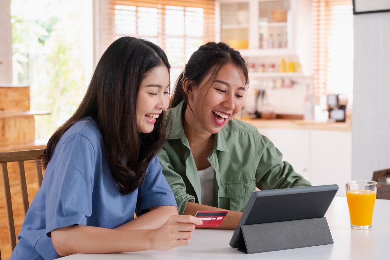 Asian couple using tablet and credit card to shop online on kitchen table at home.