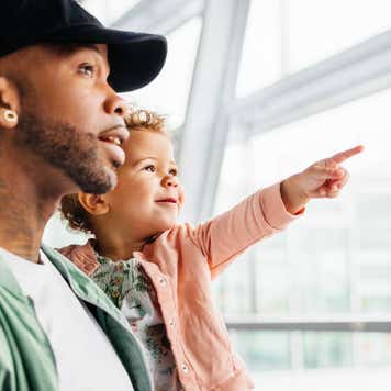 A man holds his child up to a window while the child points outside.