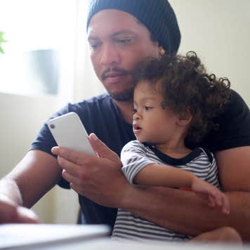 Man works on laptop while holding a child