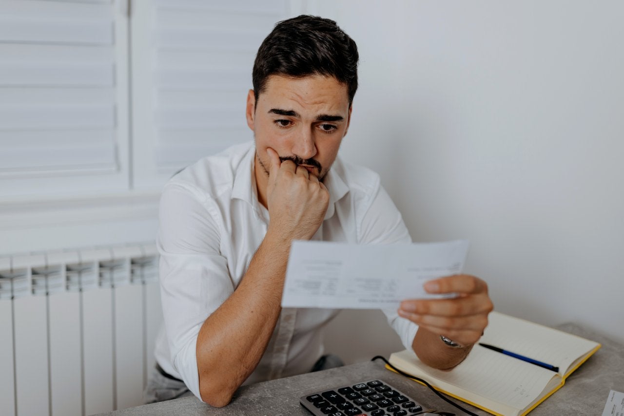 A worried mid-adult man stares at the electricity bill in front of him and wonders if he will have enough money to pay for everything