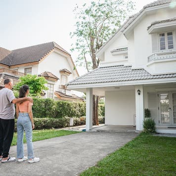 A three-member family is seen in the front of their house, looking at their home, pleased to be homeowners.