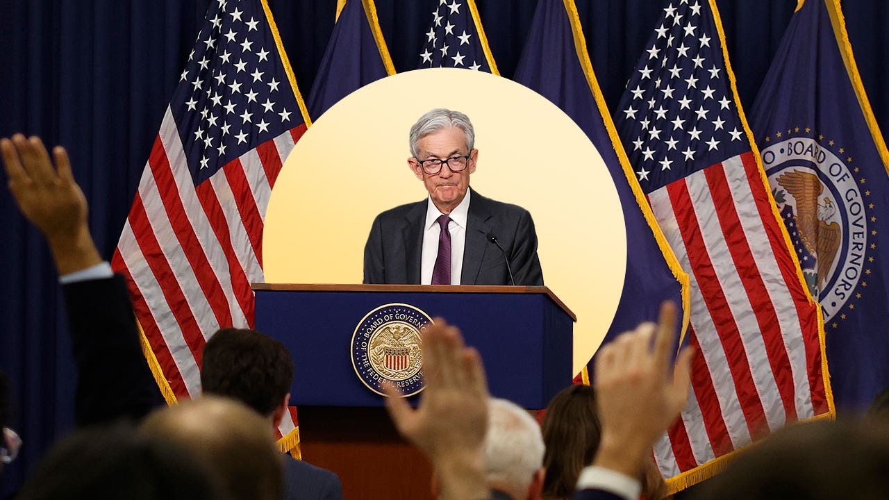 Image of Jerome Powell standing behind a podium with American flags behind him.