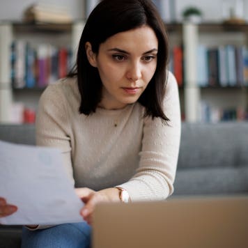 Woman reviewing financial documents while sitting at her laptop at home