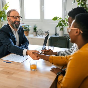 Grateful couple handshake with mortgage lender before signing contract