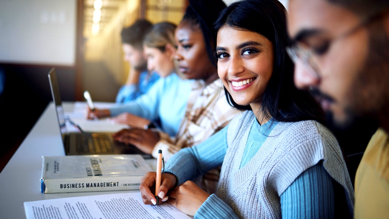 College student writing notes for business management in classroom, course and campus. Portrait, young indian girl and university student happy for learning, education and studying at finance academy - stock photo